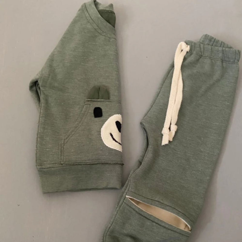 The Khaki Bear Tracksuit is not just an ordinary one. It has been designed with comfort, style and play time in mind. Front pocket has bear face detail, and the legs has soft cushion openings which provides extra cushioning when little one is crawling or sitting.

Colour - Khaki Melange