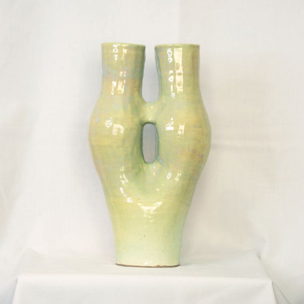 A Tall coil build stoneware vase extending into two necks covered with a melon green glaze.