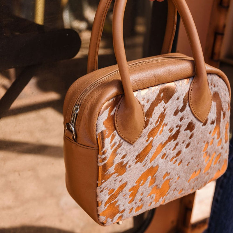 A limited-edition bag with only 10 pieces made. This exclusive design features exotic Nguni hair-on leather with delicate metallic gold splashes, beautifully complemented by a caramel leather back, bottom and sides.